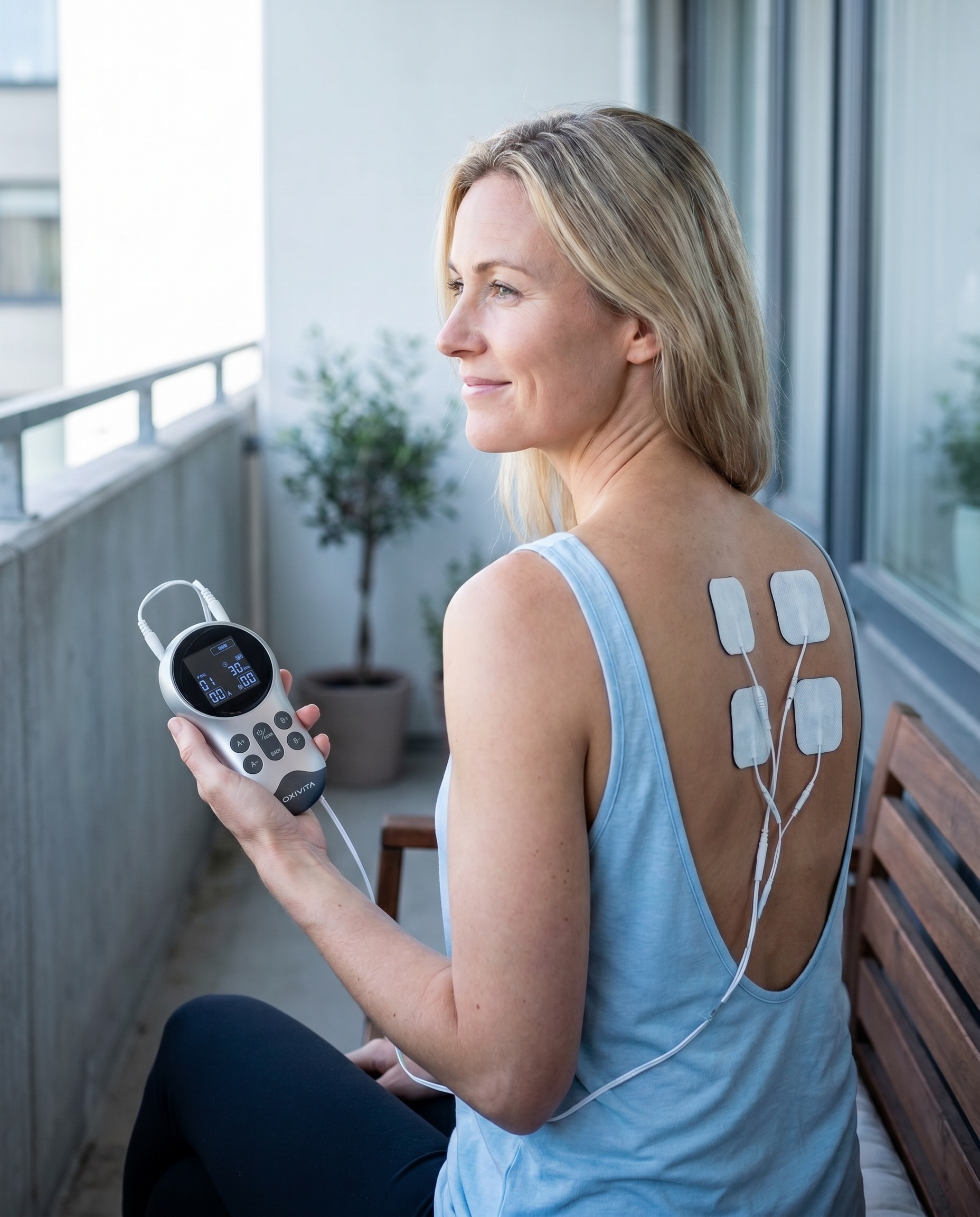 Kvinna använder Oxivita Pulse T1 TENS-apparat med elektroder på ryggen mot ryggsmärta på balkongen